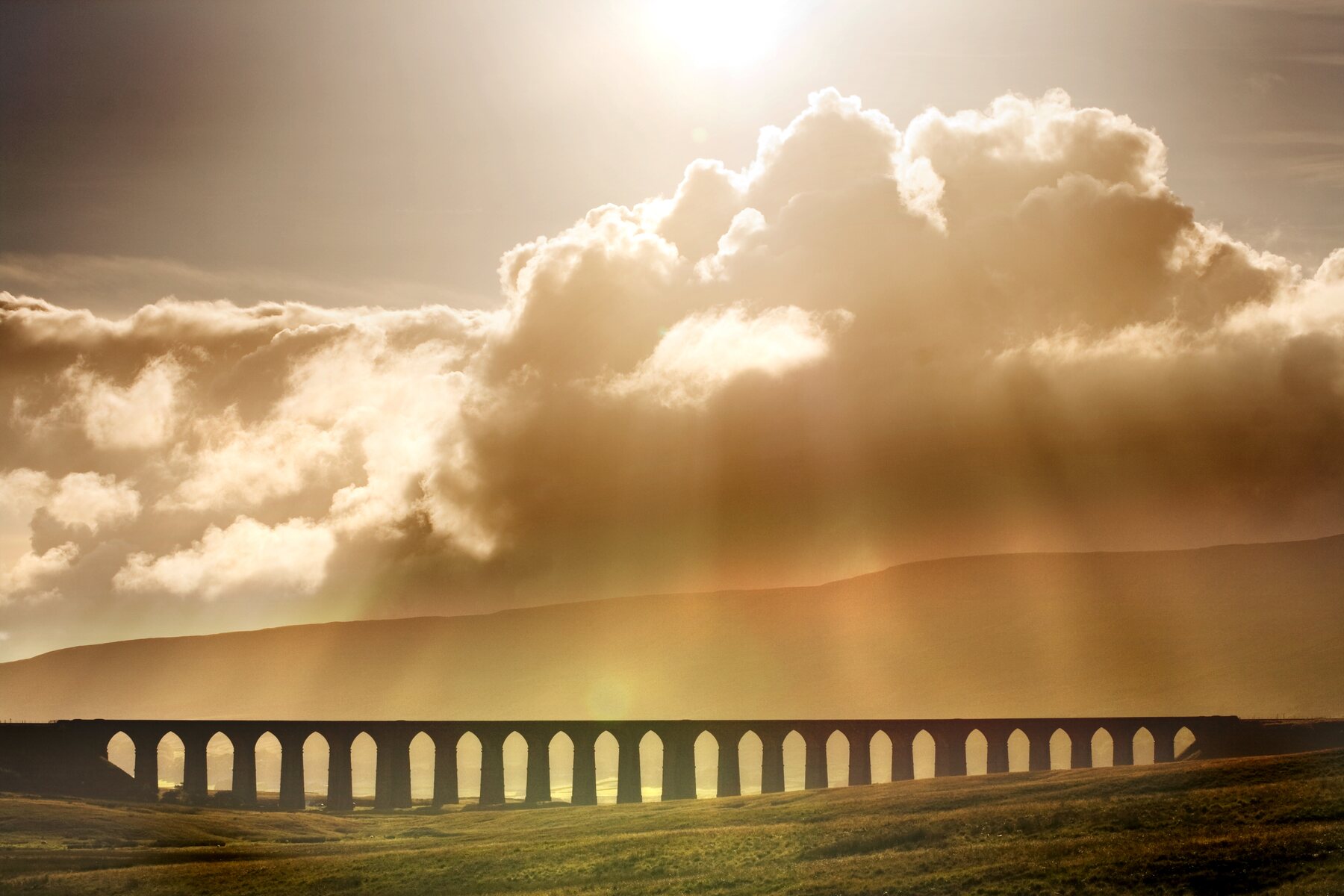 Ribblehead Viaduct crossing a sunlit Yorkshire Dales landscape beneath dramatic clouds